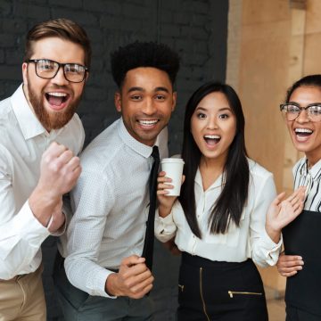 Photo of happy excited young business colleagues indoors coworking. Looking camera make winner gesture.